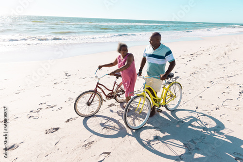 High angle view of african american senior couple with bikes talking and walking at beach in summer