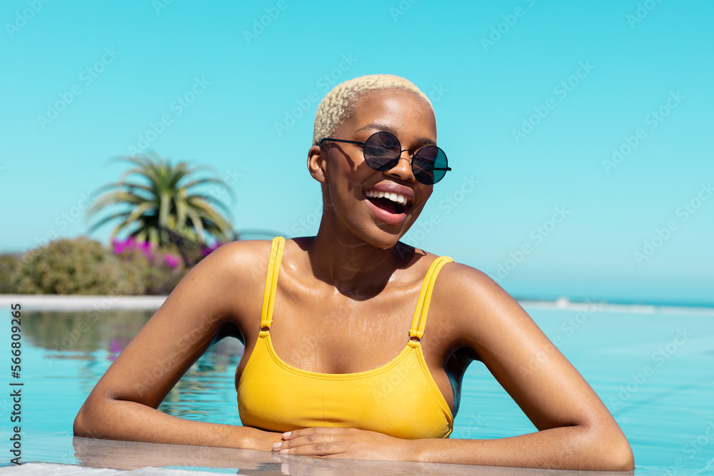 Portrait of happy african american woman wearing sunglasses in swimming pool