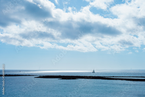 Seascape and cloudscape in blue color. Calm sea on a sunny day with clouds horizontal landscape background.  Distant boat silhouette in the ocean. © Dina