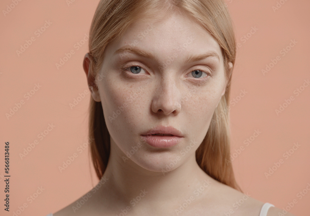 Portrait of beautiful 20s fashion model Caucasian female with no make-up posing, looking into camera against light brown pastel colored background Portrait of beautiful 20s fashion model Caucasian female with no make-up posing, looking into camera against light brown pastel colored background