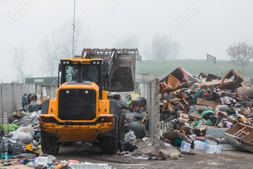 Front loader with scrap handling grapple bucket moving forward and backward to push, scoop and dump material at recycling and waste center