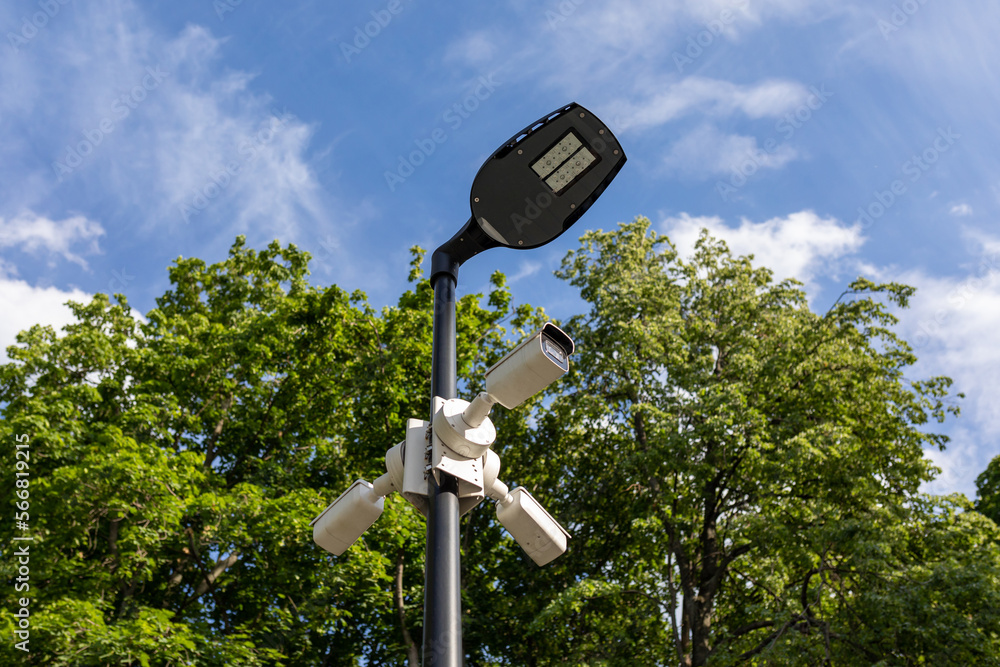 Modern lamppost and 3 surveillance cameras mounted in different directions in public park. Public space security systems Modern lamppost and 3 surveillance cameras mounted in different directions in public park. Public space security systems