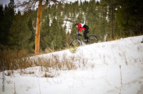 A male mountain biker in winter riding clothing riding a snow bike or 