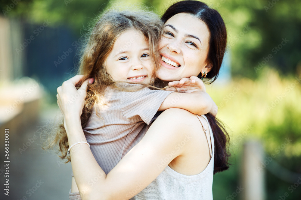 Little daughter hugging her young happy mom in the park. Little daughter hugging her young happy mom in the park.
