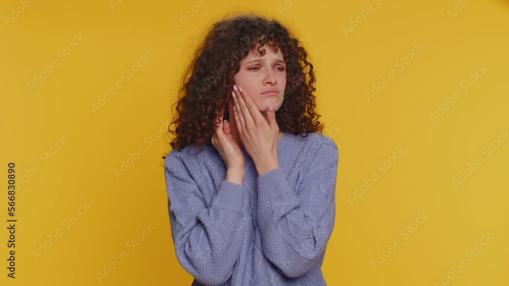 Hipster curly haired woman touching sore cheek suffering from toothache cavities or gingivitis waiting for dentist appointment gums disease. Young girl indoor studio shot isolated on yellow background Hipster curly haired woman touching sore cheek suffering from toothache cavities or gingivitis waiting for dentist appointment gums disease. Young girl indoor studio shot isolated on yellow background