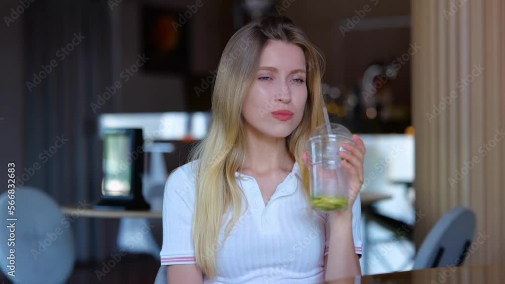 Close up of joyful young woman sitting in cafeteria and drinking ice tea. Pretty happy Caucasian female with lemonade drink in restaurant bar indoors. Real time. Leisure concept Close up of joyful young woman sitting in cafeteria and drinking ice tea. Pretty happy Caucasian female with lemonade drink in restaurant bar indoors. Real time. Leisure concept