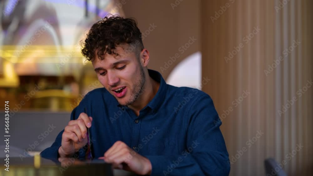 Close up of happy young man sitting in cafe indoor and eating wok food. Curly handsome Caucasian guy in modern restaurant having tasty meal. Delicious healthy food. Nutrition. Real time. Close up of happy young man sitting in cafe indoor and eating wok food. Curly handsome Caucasian guy in modern restaurant having tasty meal. Delicious healthy food. Nutrition. Real time.