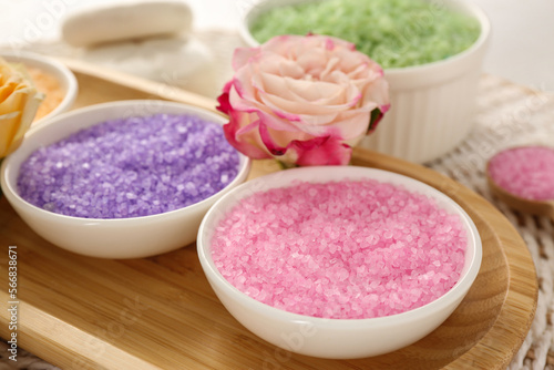 Bowls with different sea salt and beautiful rose on wicker mat, closeup