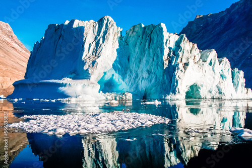 Iceberg in polar regions with blue reflections and floating ice in the foreground.