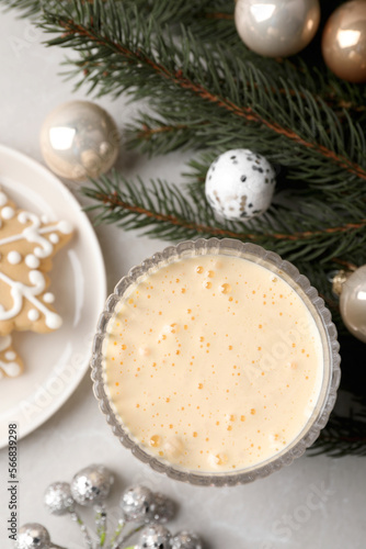 Glass of delicious eggnog  cookie and decorated fir branch on light table  flat lay
