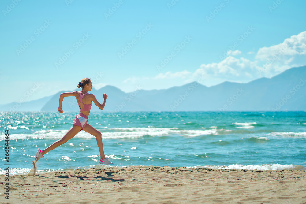 Confident athlete woman running in morning along the beach. Fit girl jogging on seashore with mountains, cardio workout training outdoors