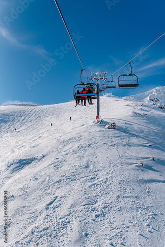 group of unrecognizable people in ski equipment, riding a chairlift up a snowy mountain on a sunny day. winter sports.