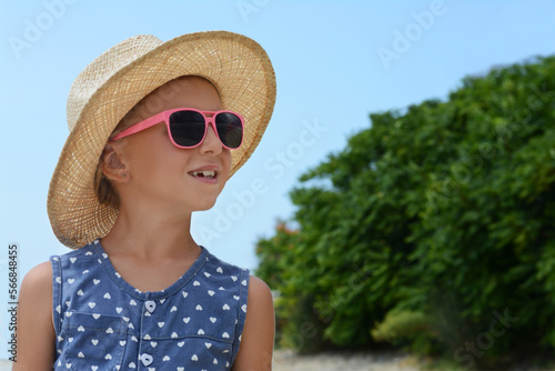 Little girl wearing sunglasses and hat at beach on sunny day. Space for text © New Africa