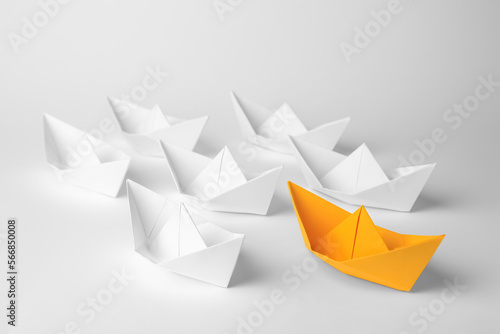 Group of paper boats following orange one on white background. Leadership concept