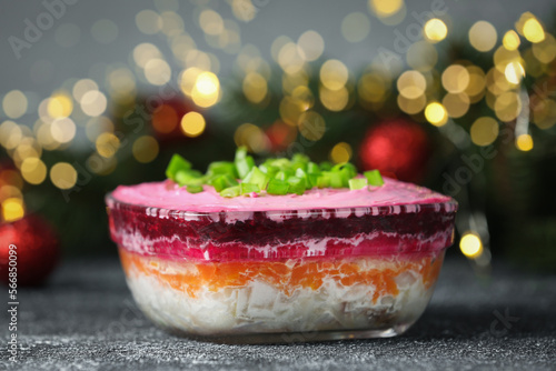 Herring under fur coat salad on grey table against blurred festive lights, closeup with space for text. Traditional Russian dish