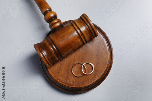 Divorce process. Wooden gavel and wedding rings on grey textured table, flat lay