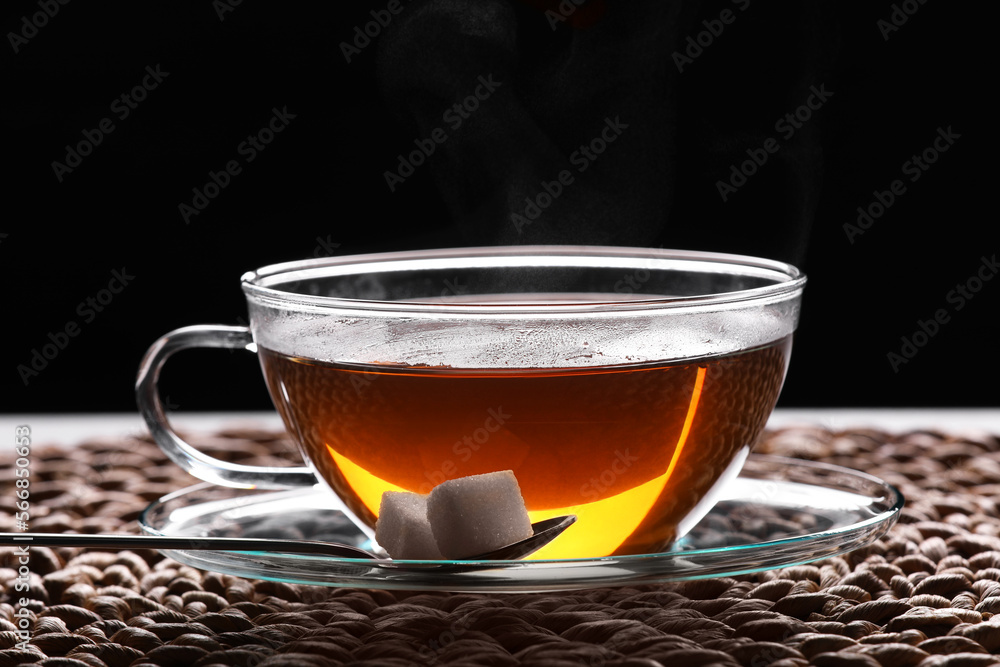 Glass cup of tea with sugar cubes on table against black background, closeup Glass cup of tea with sugar cubes on table against black background, closeup