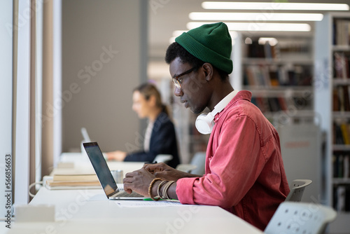 Foto Entrepreneurial independent African American man sits with laptop in library building working on launching own IT startup