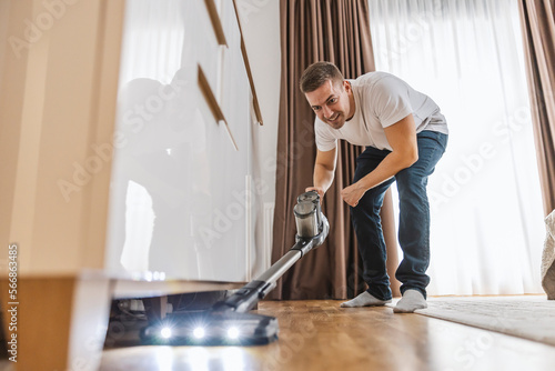 Foto A happy young man is doing chores at home and vacuuming floor.