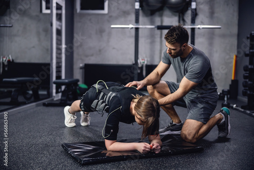 Foto A woman in a black EMS training suit laying in a plank position on her elbows in the middle of a training center