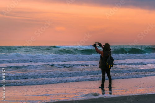 A tourist taking video of huge ocean waves in Robert Moses State Park, New York during an evening