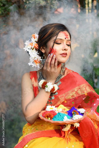 Portrait of pretty young indian girl wearing traditional saree and jewellery, holding powder colours in plate on the festival of colours called Holi, a popular hindu festival celebrated across India.