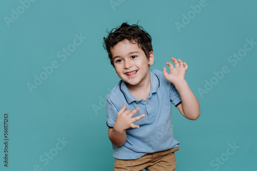 Happy curly little Italian boy in blue polo dancing, smiles against turquoise studio background. Healthy caucasian toddler enjoying life. Childhood, entertainment for kids. Caucasian baby boy smiles.