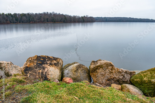 Iced over lake reservoir with boulders in foreground and forest in nbackground. photo