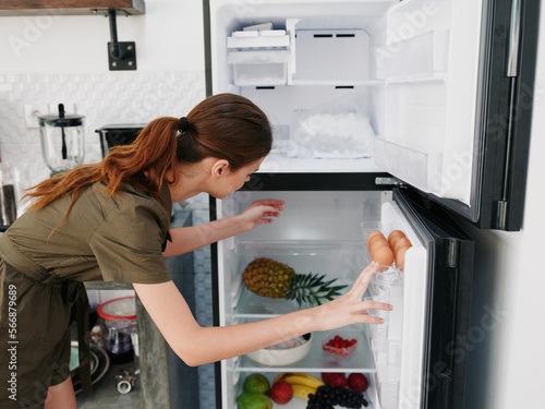 A woman opened the refrigerator and looks sadly into it, wondering what to cook, defrosted the refrigerator, freezer repair in the kitchen at home