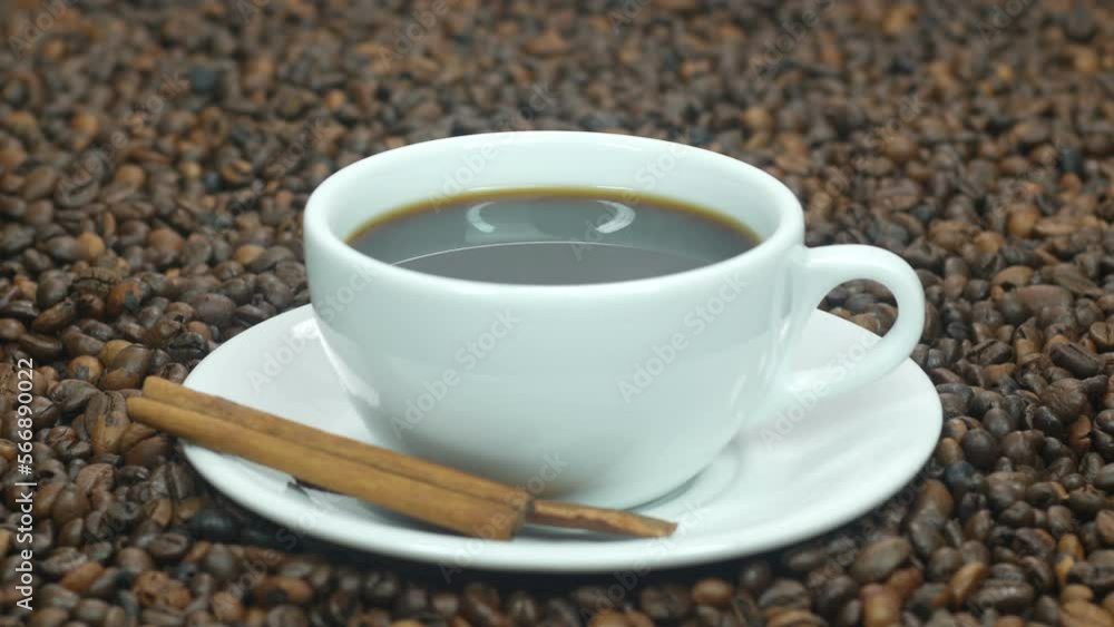 A cup of hot coffee stands on the table next to coffee beans. Cinnamon sticks for coffee are very tasty. Coffee beans background for advertising. A cup of hot coffee stands on the table next to coffee beans. Cinnamon sticks for coffee are very tasty. Coffee beans background for advertising.