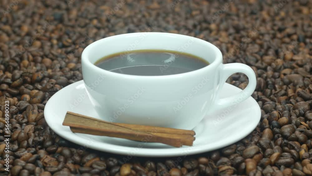 A cup of hot coffee stands on the table next to coffee beans. Cinnamon sticks for coffee are very tasty. Coffee beans background for advertising. A cup of hot coffee stands on the table next to coffee beans. Cinnamon sticks for coffee are very tasty. Coffee beans background for advertising.