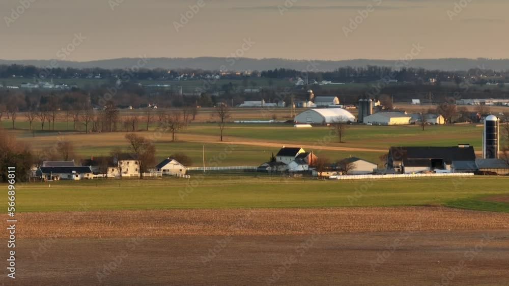 Long aerial panning zoom of Amish farm and home. Beautiful winter golden hour sunset shines on rural farmland in Lancaster, PA.