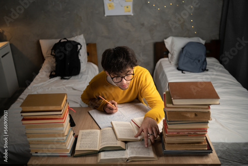 Serious male student writing, reading books and prepare for college exam in dormitory room. Top view. photo