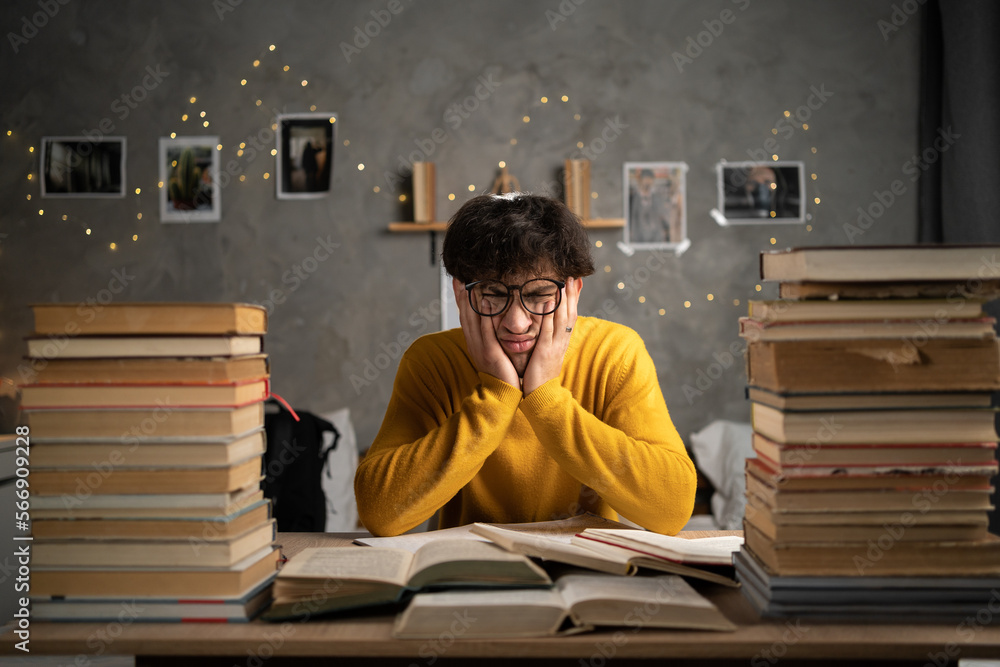 Student studying hard exam with books, tired guy read difficult book in dormitory. - obrazy, fototapety, plakaty 