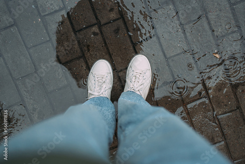 Fototapeta the legs of a woman in a puddle in a white sneakers and a blue jeans