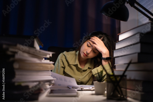 Portrait of Asian Businesswoman sitting and working hard at with front of computer and lots of documents on the table in workplace at late with serious action, Work hard and too late concept