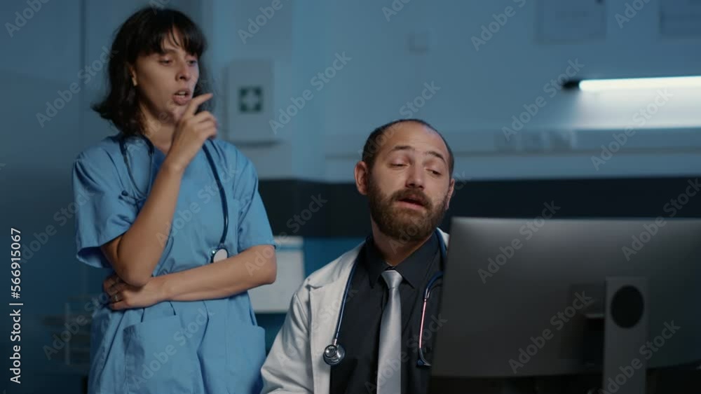 Doctor and assistant looking at patient medical expertise on computer discussing illness symptoms planning medication treatment. Clinical staff working after hours in hospital office. Medicine concept Doctor and assistant looking at patient medical expertise on computer discussing illness symptoms planning medication treatment. Clinical staff working after hours in hospital office. Medicine concept