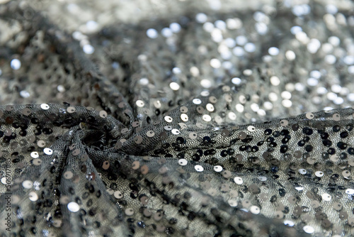 defocused black and silver knitted fabric with sequins and folds texture background 