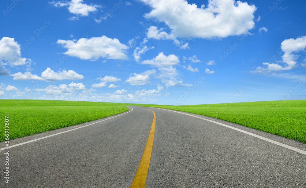 Tarmac road in slope grass field with blue sky background.
