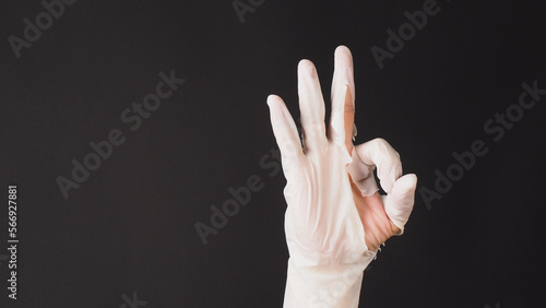 Ok hand sign and wear latex glove on black background.