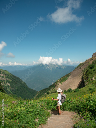  Female hiker with backpack and trekking poles hiking in mountains enjoying the scenic view during sunny day