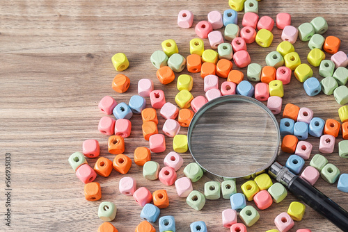 A magnifying glass surrounded by colorful cubes on the wooden table. 