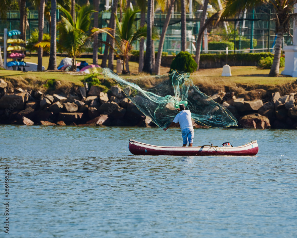 Fototapeta premium fisherman in his canoe using a net to fish in the middle of the sea