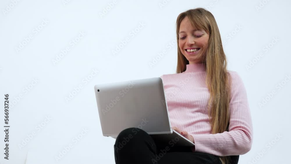 A young beautiful woman is sitting on a chair and writing down or taking down notes while attending an online video class or office meeting on a laptop in an interior house. Work from home