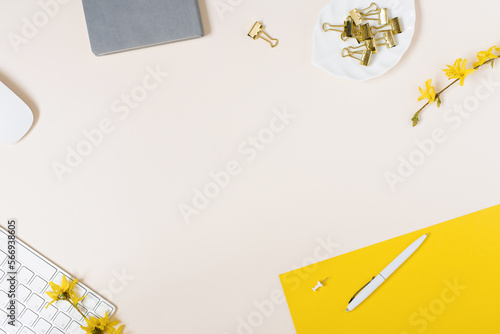 On a light background flat lay with a yellow flower, a notepad keyboard and paper clips, a female floral desktop. The concept of a stylish spring or summer morning. Top view and copy space