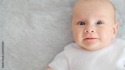 Child's face of a Happy newborn baby looking to camera. Healthy newborn baby in a white t-shirt with blue eyes. Face of a Beautiful active tiny child. Cute white Infant boy, top view.