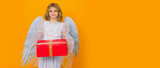 Angel child hold gift present. Cute angel kid, studio portrait. Banner header, copy space. Blonde curly little angel child with angels wings, isolated background.