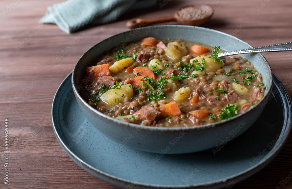 Lentil soup or stew. Cooked with vegetables, potatoes and pork meat isolated on wooden table. Closeup and front view Lentil soup or stew. Cooked with vegetables, potatoes and pork meat isolated on wooden table. Closeup and front view