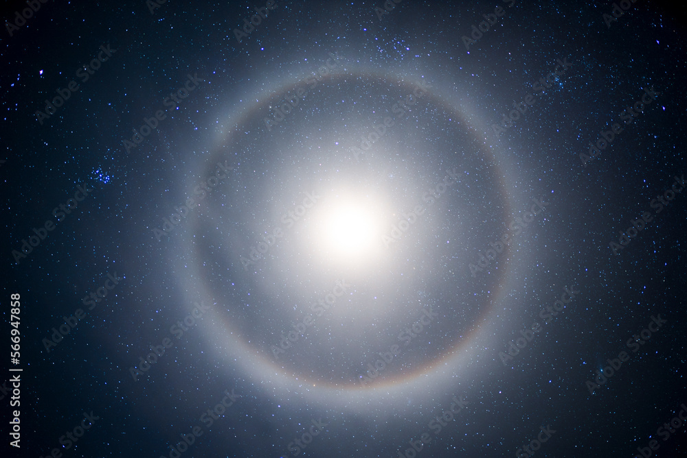 halo from the moon in the starry sky at night. A lunar halo around the Moon, showing several color bands in its iridescent form, in early winter. long exposure. - obrazy, fototapety, plakaty 