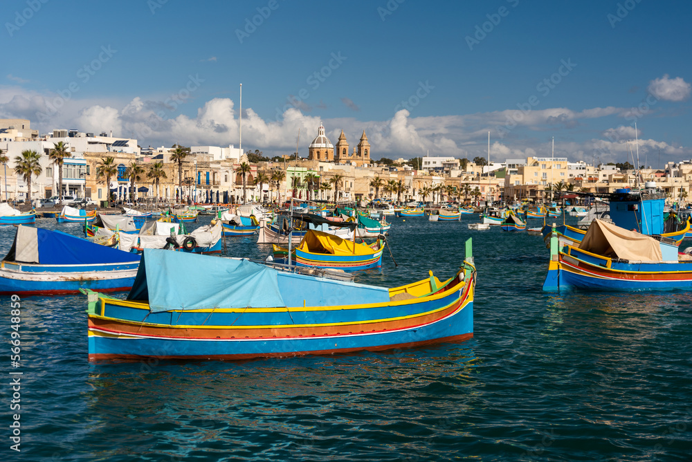 Old Colorful Boats Luzzu in Marsaxlokk harbor at sunny day. Blue sky with clouds